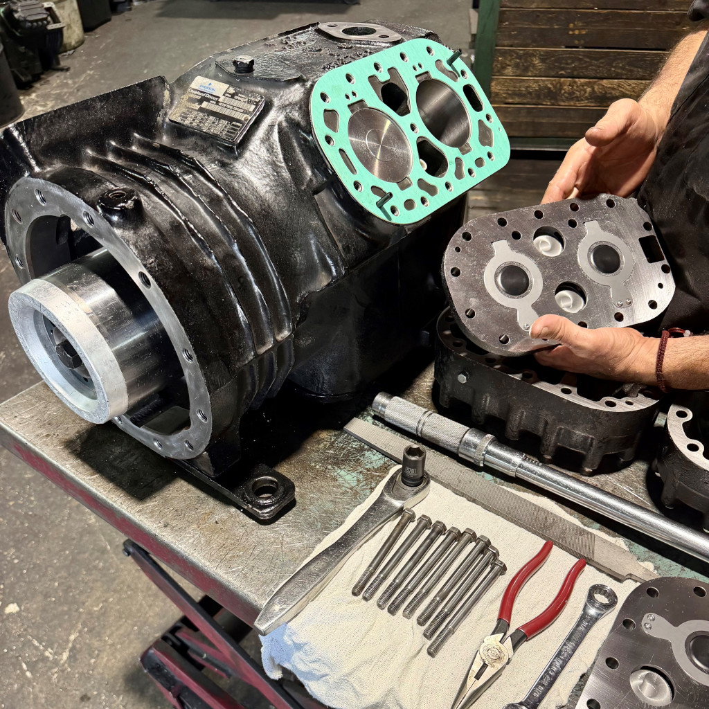 Technician handling disassembled commercial compressor components on a workbench